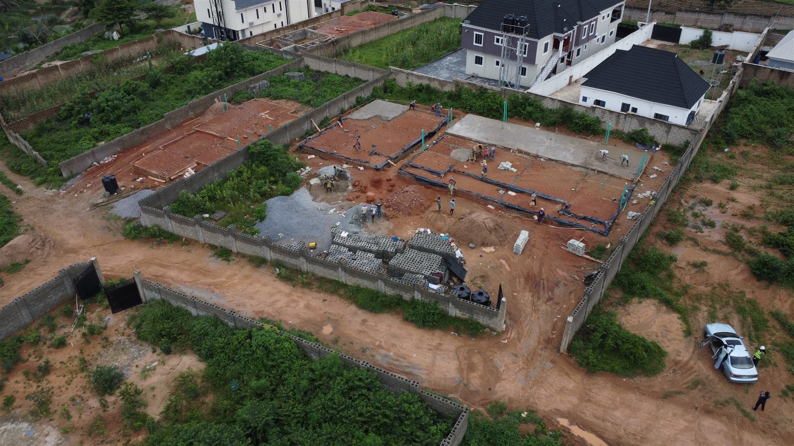 Aerial view of the Eden site at weeks 7 and 8: damp-proof membrane laid and fresh concrete ground-floor slabs being cast across the three homes