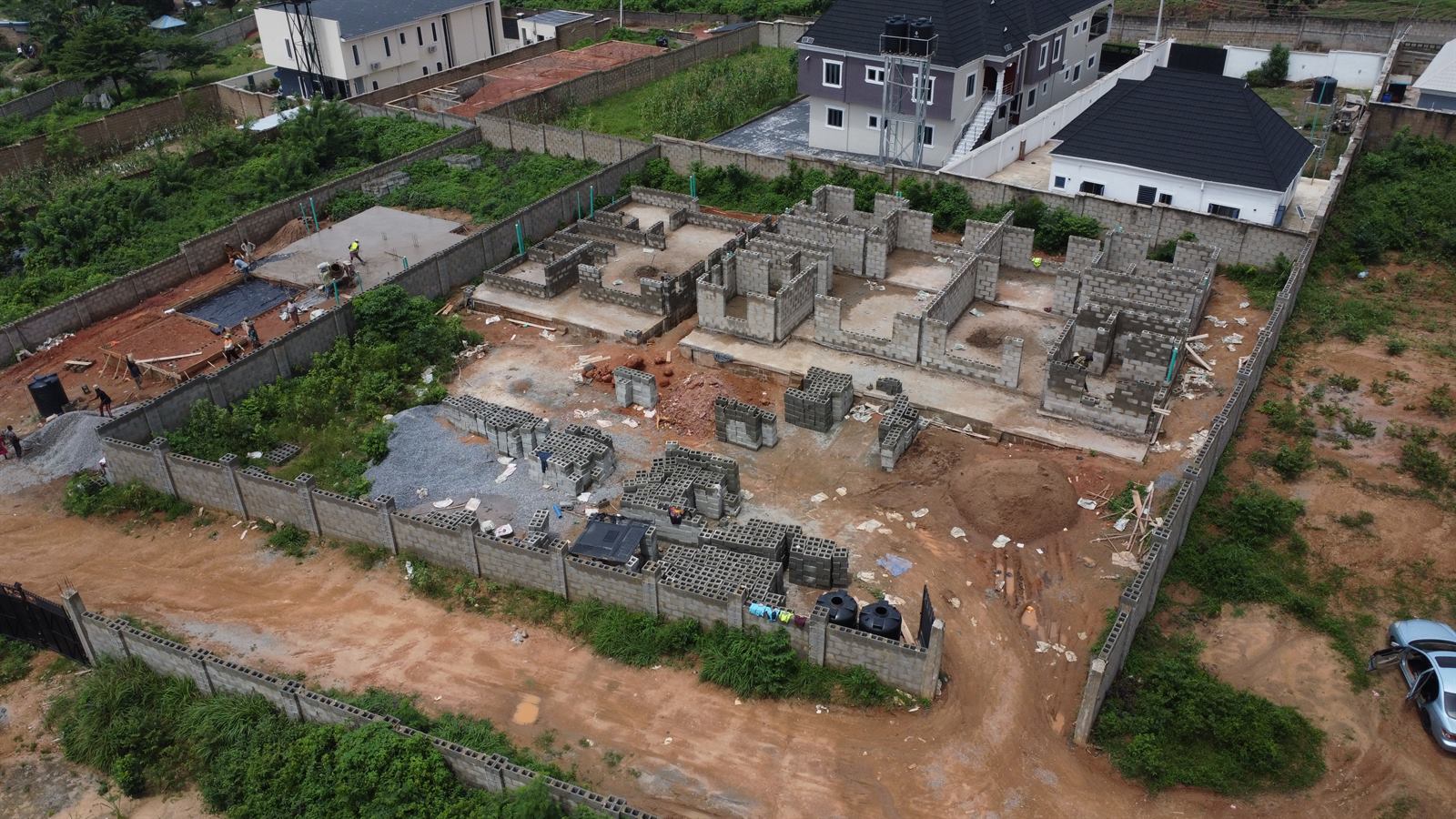 Aerial view of the Eden site at week 9: ground-floor blockwork rising on all three homes, with the final slab being cast in the corner of the site